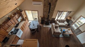 Amplia sala de estar con chimenea de piedra, mobiliario de madera y cocina con armarios de madera.