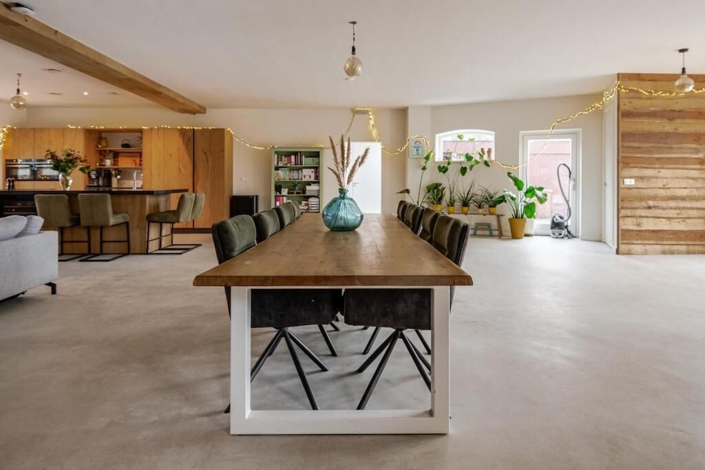 Amplia sala de estar con una larga mesa de madera para comer, una cocina al fondo y un rincón de estar acogedor.