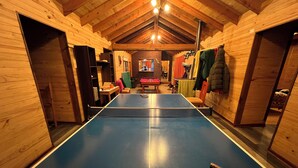 Ein Tischtennistisch in einem Raum mit Holzwänden und einer hohen Decke, ein Billardtisch und ein Kamin.