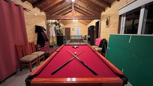 Ein Billardtisch in einem Holzraum mit hoher Decke und Blick auf eine Tür, die nach draußen führt.