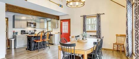 A dining area with a wooden table and chairs, a kitchen with modern appliances, and a red door.