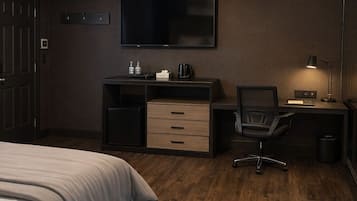 A hotel room with a bed, a desk with a chair, a flat-screen TV, and a desk lamp.