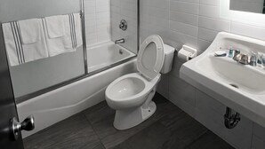 A modern bathroom with a glass-enclosed shower, a white toilet, and a sink with a mirror. - Stella Hotel Bronx (Bronx)