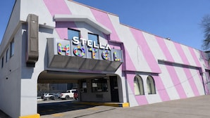 A hotel with a distinctive pink and white striped facade, a prominent sign reading 'STELLA HOTEL,' and a parking lot with several vehicles. - Stella Hotel Bronx (Bronx)