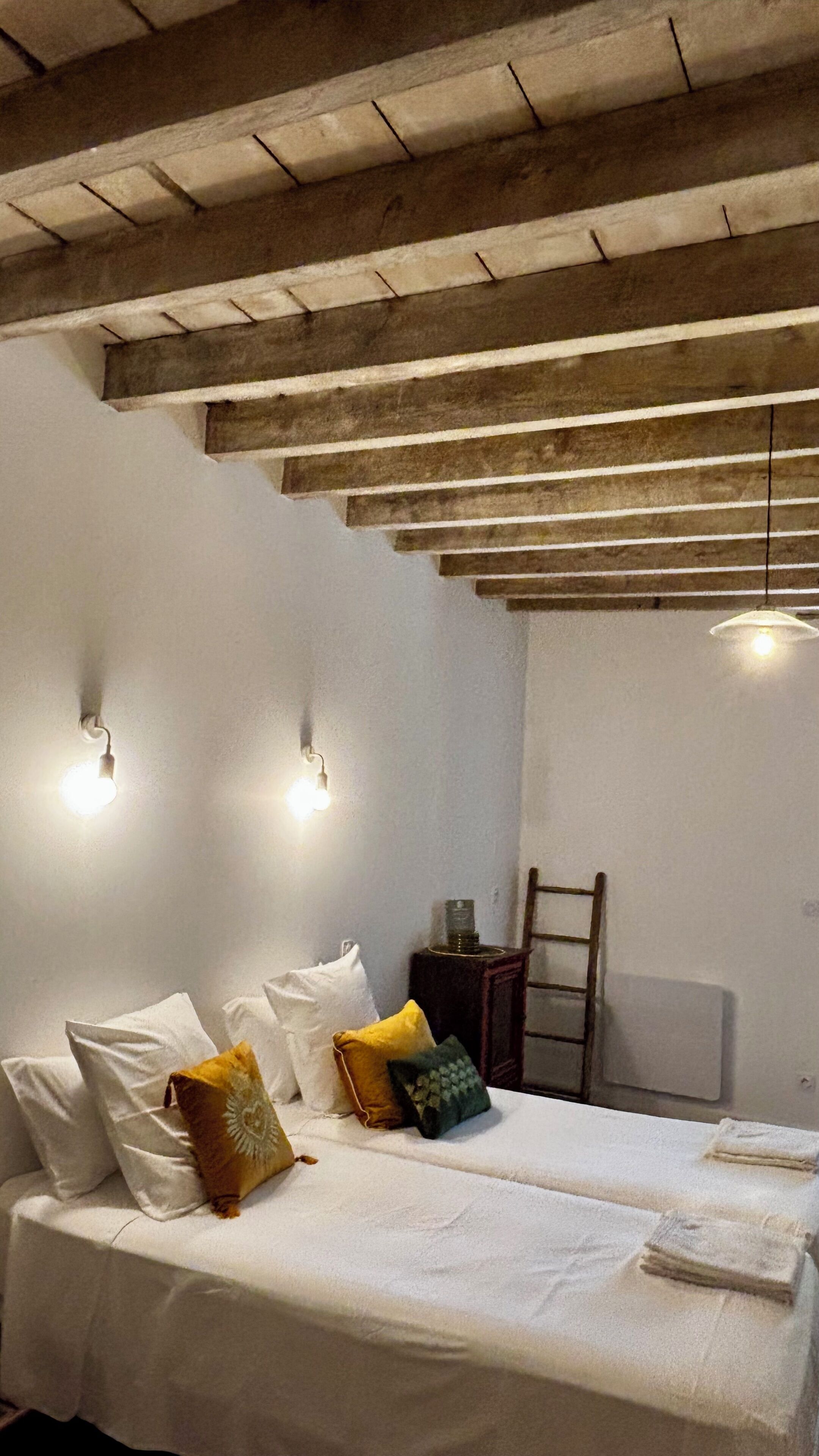 Une chambre à coucher avec un lit, des oreillers, une table de chevet, une chaise et un luminaire suspendu.