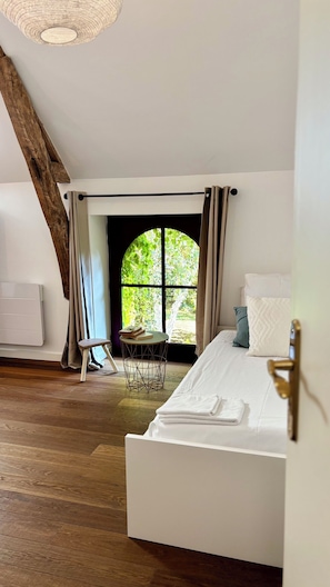 A bedroom with a large window, a bed, a radiator, and a wooden floor. - LE DOMAINE DU PETIT TERTRE (Sainte-Sabine-sur-Longève)