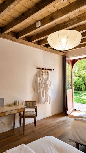 Une chambre avec un plafond en bois, un luminaire suspendu, un lit, une table de chevet, une chaise et une fenêtre donnant sur un paysage verdoyant.