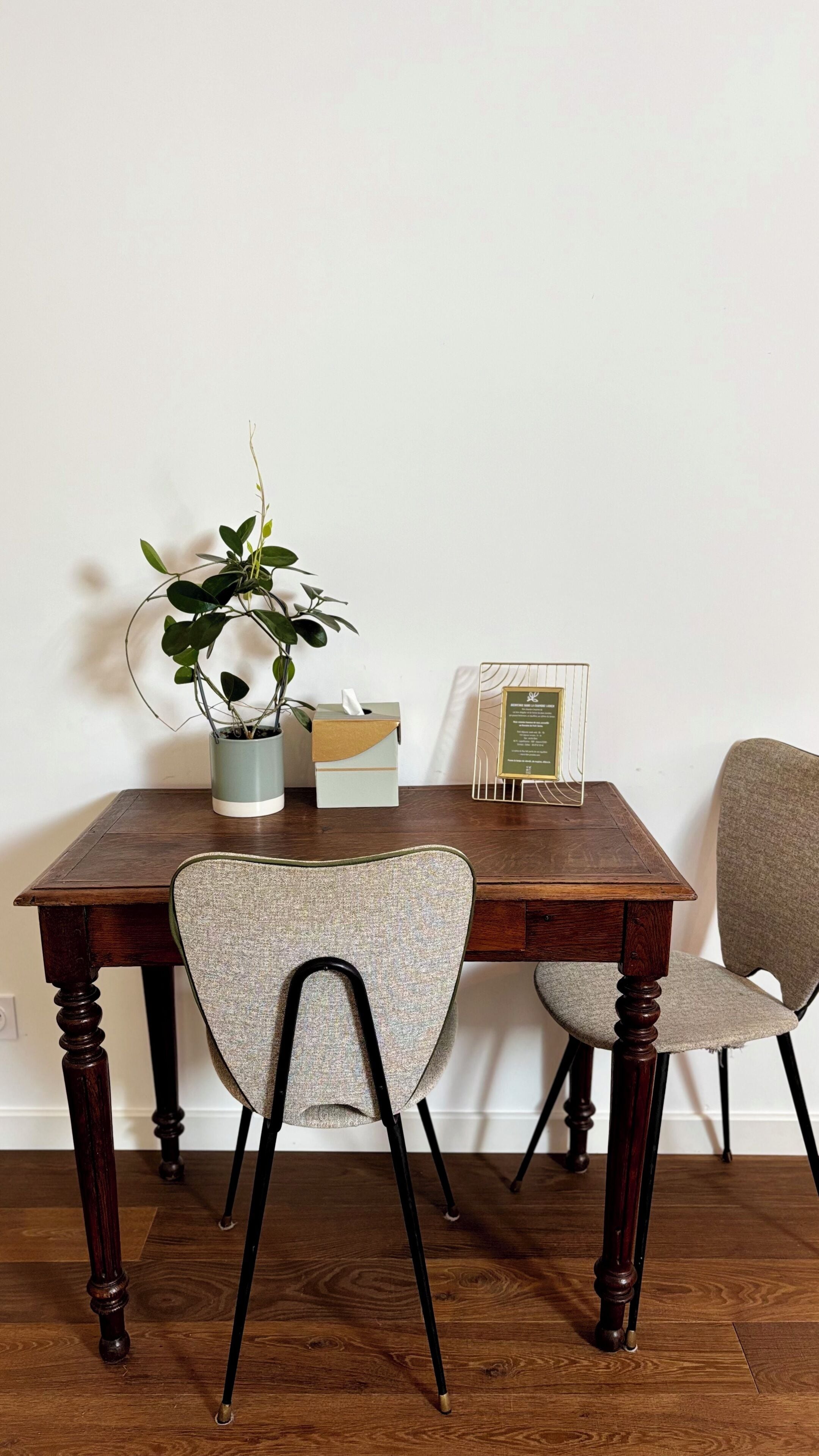 Una mesa de comedor de madera con dos sillas, una planta en maceta, una caja de pañuelos y un certificado enmarcado.