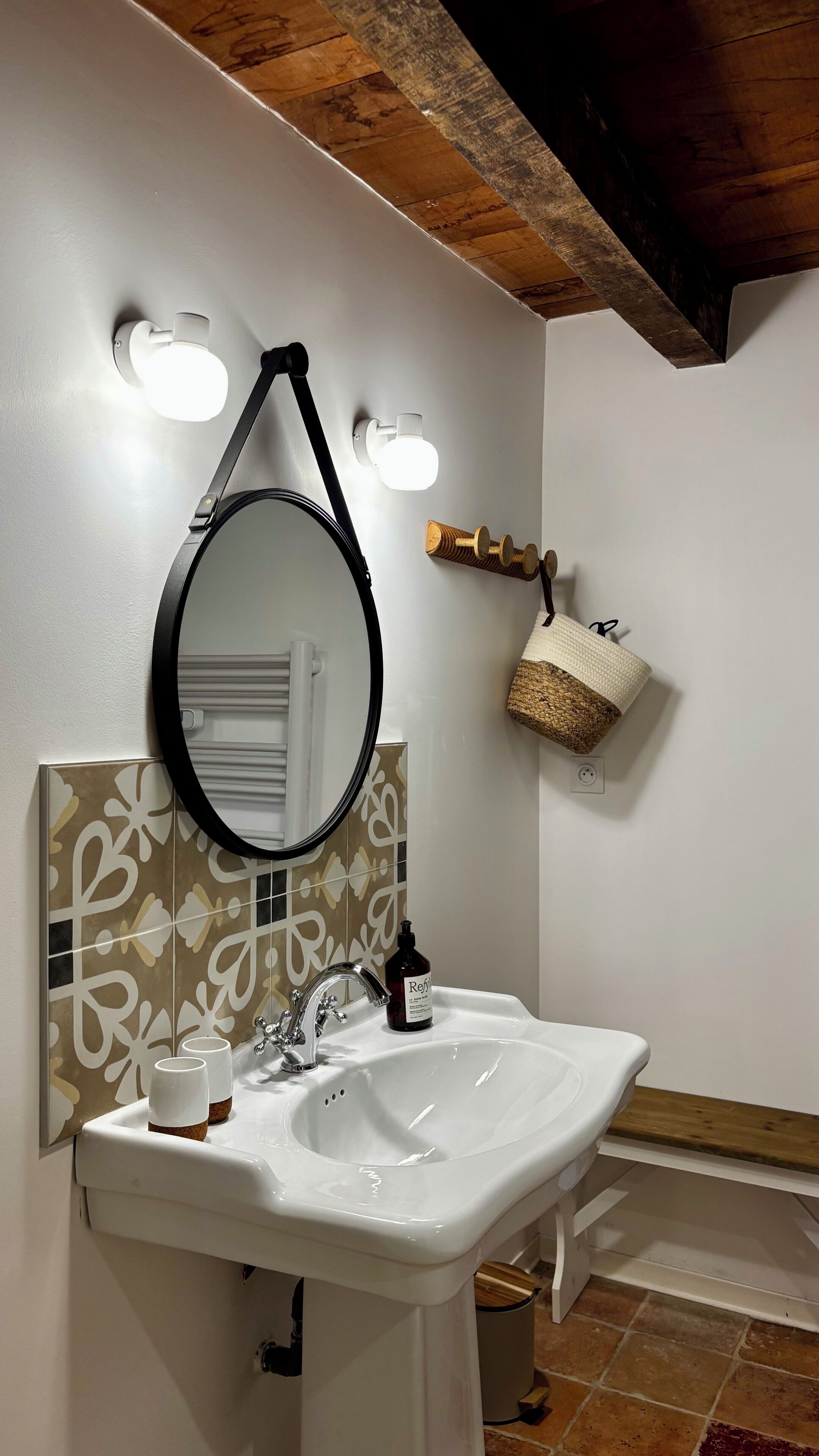 Une salle de bain avec un lavabo blanc, un miroir rond et un porte-serviettes.
