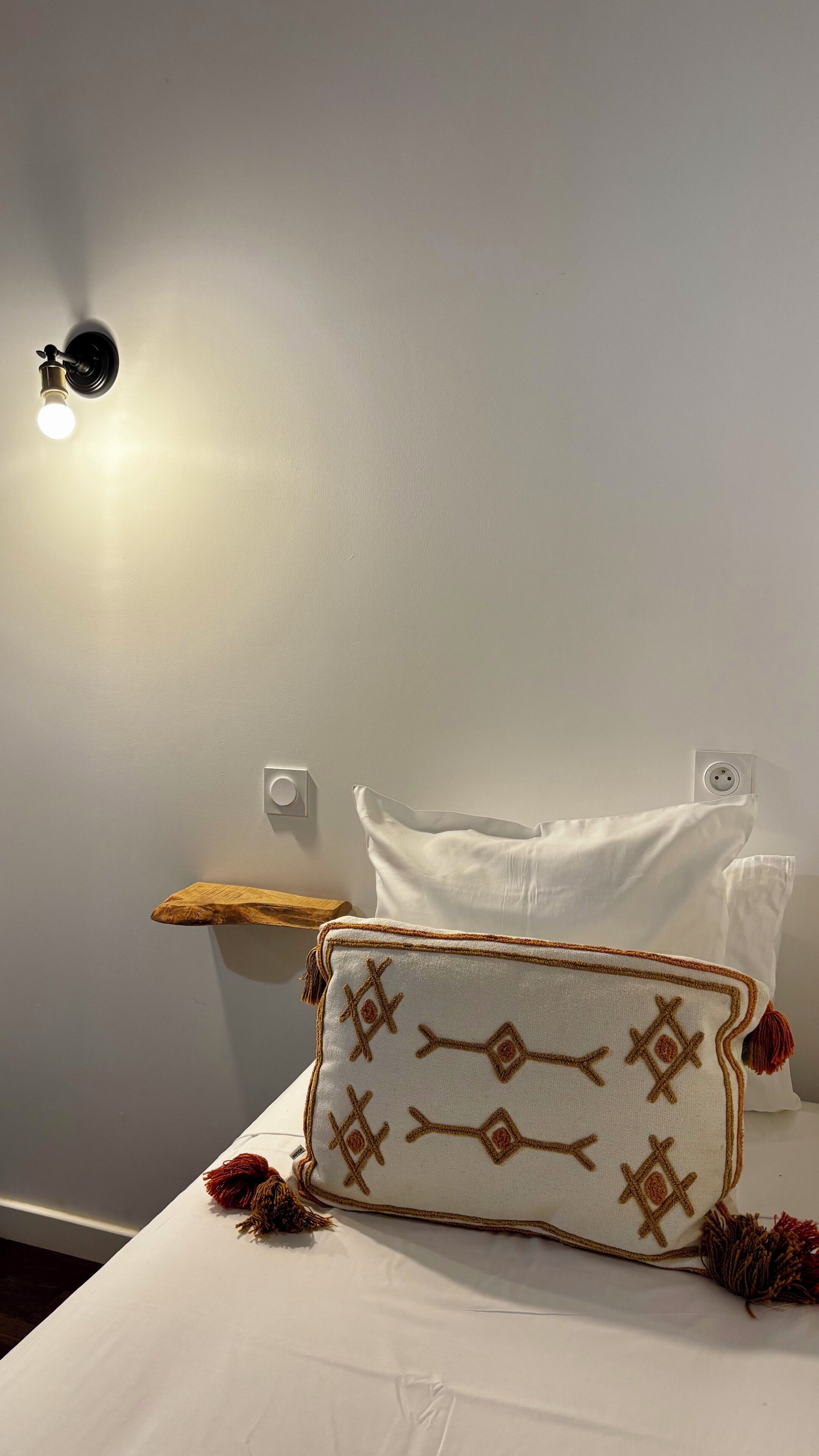 Un lit avec un oreiller blanc et un coussin décoratif orné de glands.