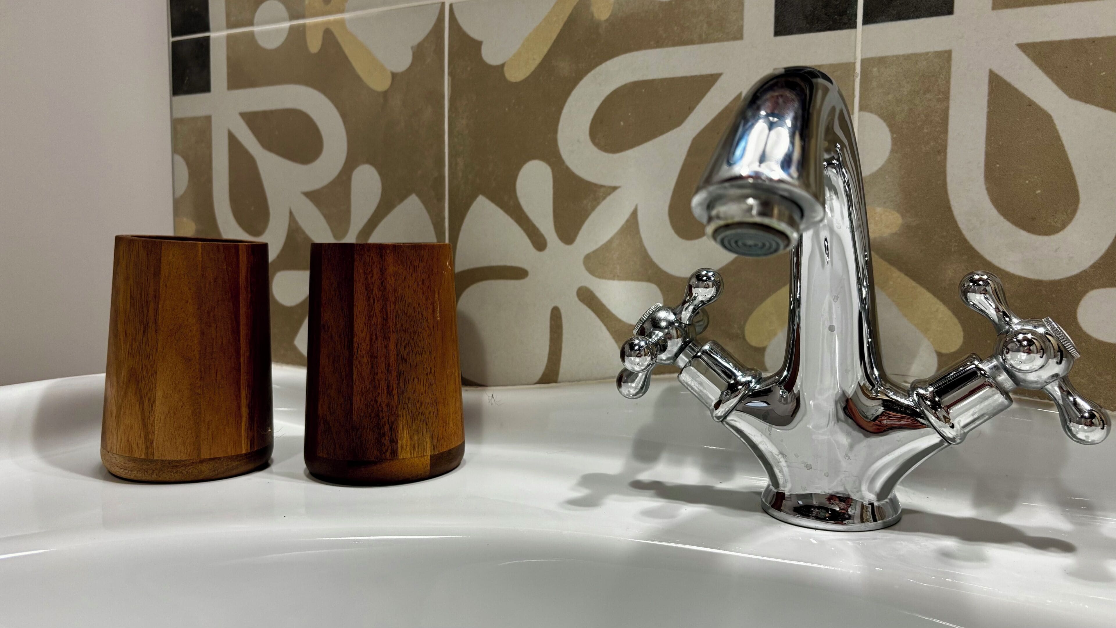 A bathroom with a chrome faucet, two wooden cups, and a patterned wall.