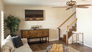 A living room with a sofa, a coffee table, a TV, a cabinet, a staircase, and a ceiling fan. - Charming 2-Bedroom Townhome Attached Garage Near Downtown Georgetown (Georgetown)