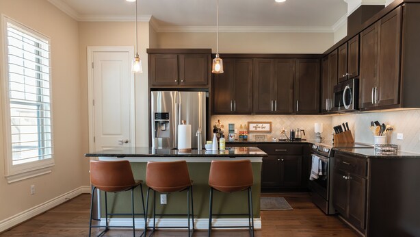 A kitchen with dark wooden cabinets, stainless steel appliances, a bar area with stools, and a window with blinds. - Charming 2-Bedroom Townhome Attached Garage Near Downtown Georgetown (Georgetown)