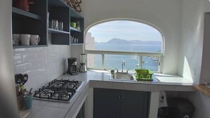 Eine Küche mit Gasherd, einer Kaffeemaschine, einem Spülbecken und einem Fenster mit Meerblick.