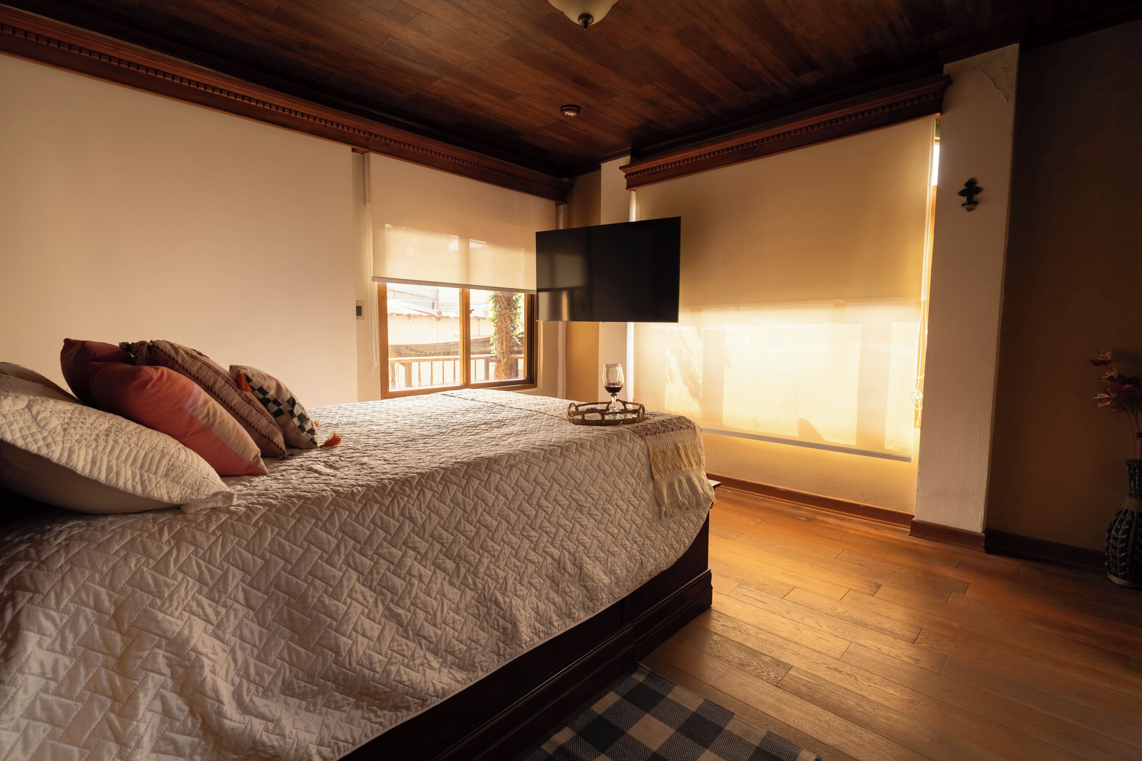Ein Schlafzimmer mit einem großen Bett, Holzboden, einem Flachbildfernseher und einem Fenster mit Jalousien.