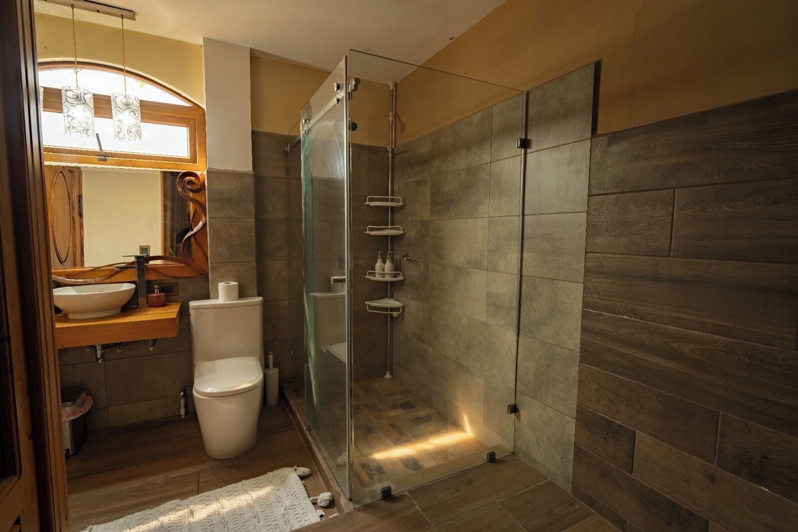A modern bathroom with a glass-enclosed shower, a wooden vanity, and a toilet.