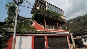 A building with a red and white facade, a black garage door, and a balcony with greenery. - CASA DARA, with a view of the Mayan Face Mountain and Lake Atitlán! (San Juan La Laguna)