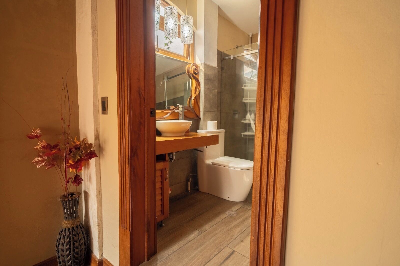 Un baño con tocador de madera, lavamanos blanco, inodoro y zona de ducha.