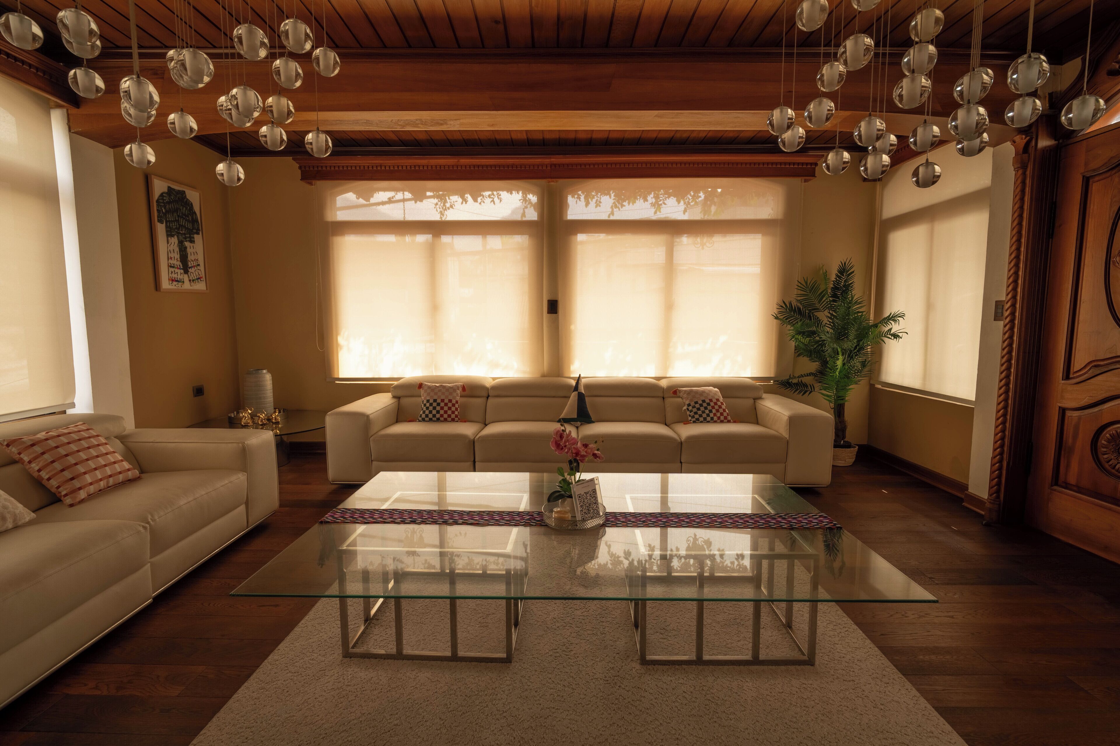 Un salon avec une table basse en verre, deux canapés, une plante en pot et des luminaires sphériques suspendus au plafond.