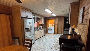 A kitchen with wooden cabinets, a refrigerator, a dining table with chairs, and a ceiling fan.