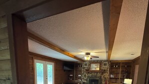 A log cabin interior with a stone fireplace, wooden floors, a leather sofa, and a ceiling fan.