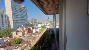 Ein Balkon mit Blick auf eine Stadtlandschaft, darunter Wolkenkratzer und ein klarer Himmel.
