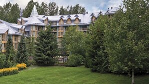 Un grande edificio a più piani con una facciata simmetrica, circondato da un'abbondante vegetazione e un prato curato.