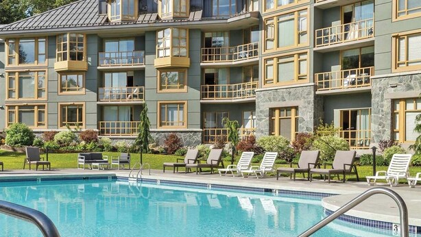 Un hotel a più piani con piscina, area salotto all'aperto e vista sulle montagne.