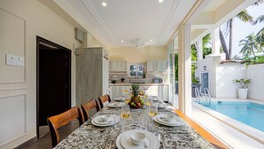 Un espace repas avec une table en marbre, des chaises et une vue sur une piscine.