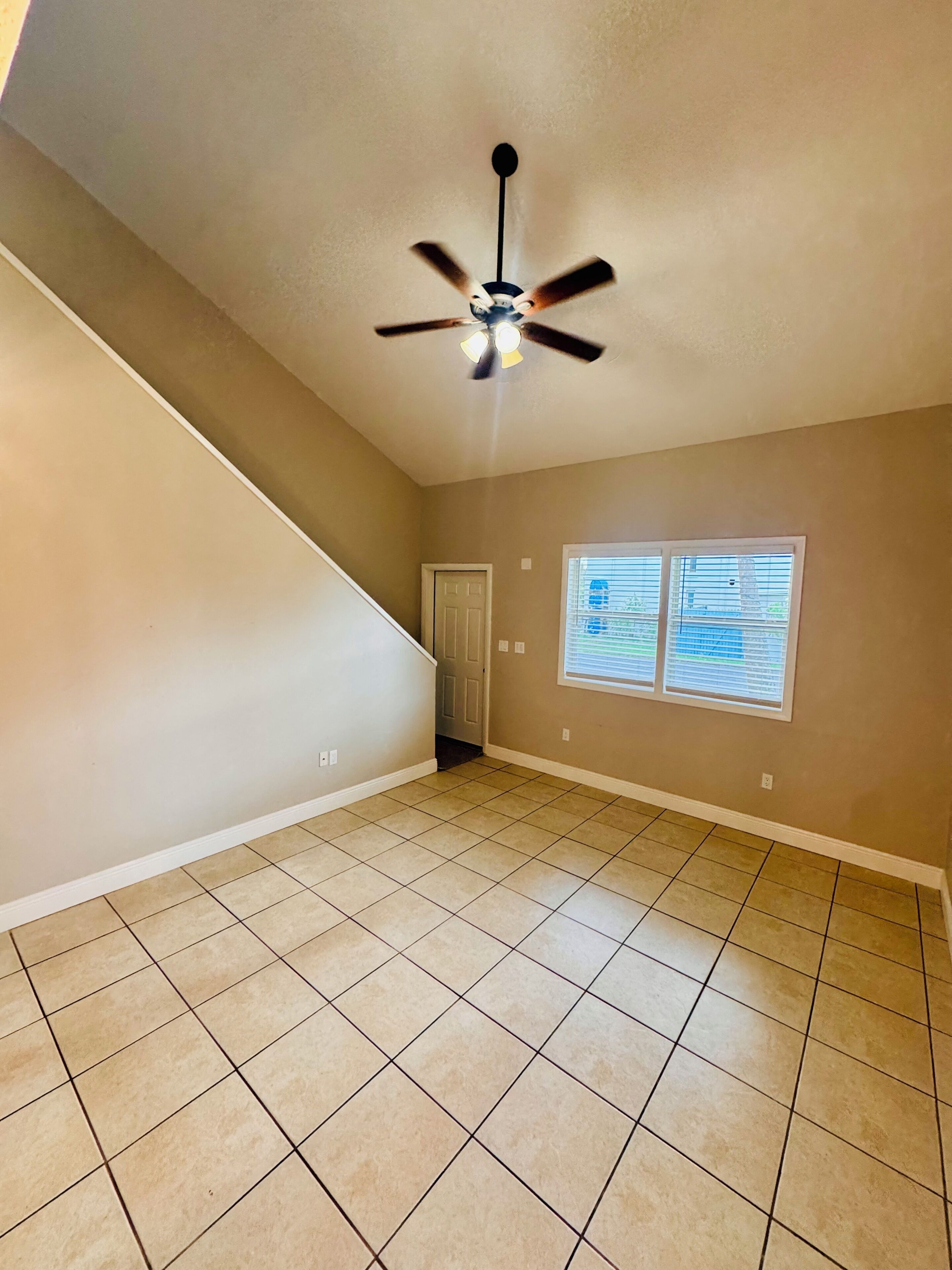 A room with a sloped ceiling, a ceiling fan, a door, and two windows with blinds.