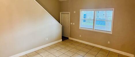 A room with a sloped ceiling, a ceiling fan, a door, and two windows with blinds.