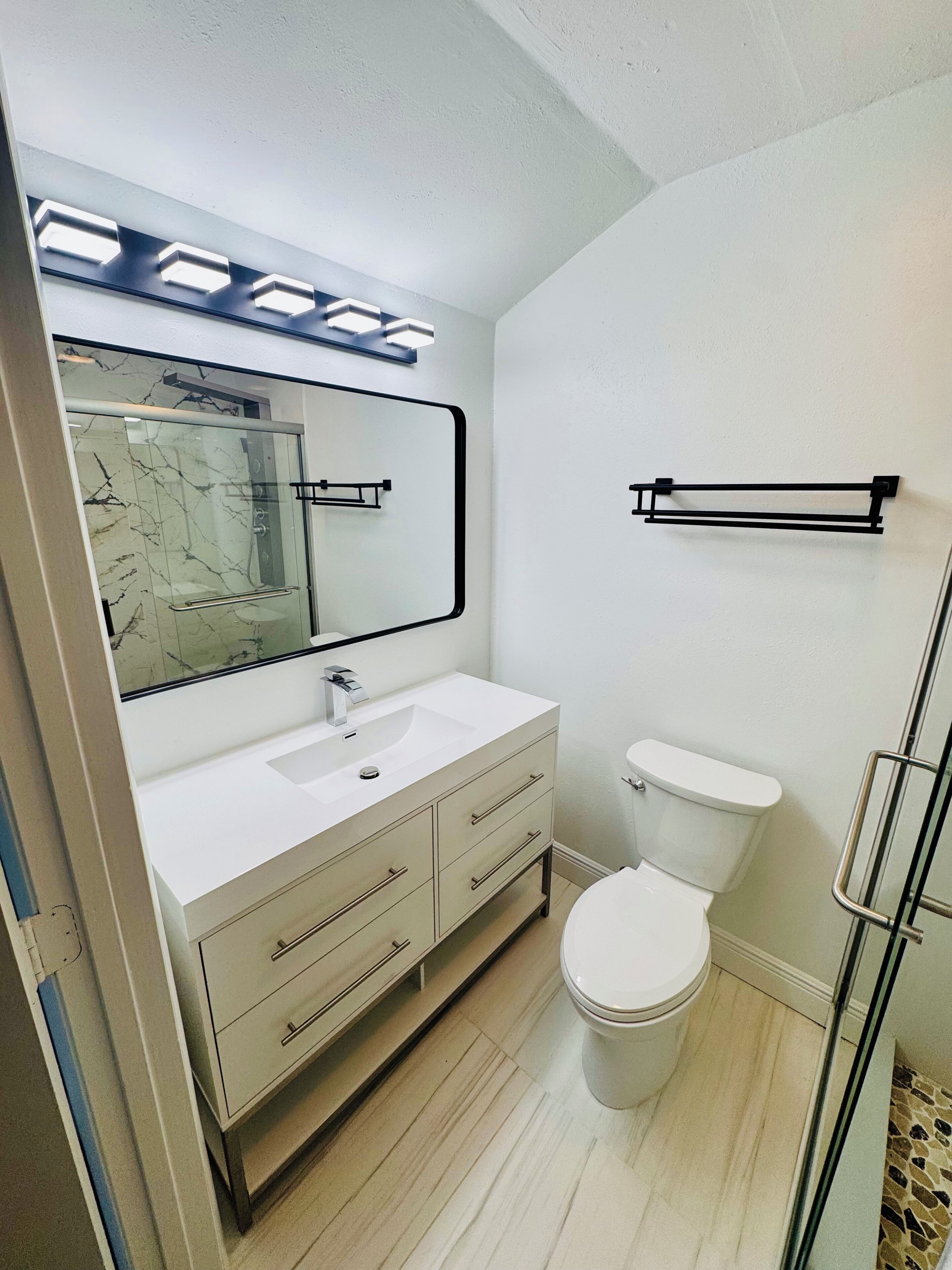 A bathroom with a white sink, a mirror, a toilet, and a shower area.