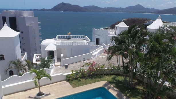 Un bâtiment blanc avec une piscine, entouré de palmiers et offrant une vue sur la mer.