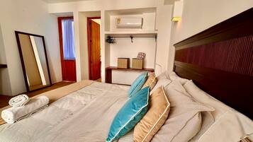 A hotel room with a large bed, a wooden headboard, a mirror, a wardrobe, and a small shelf with decorative items.