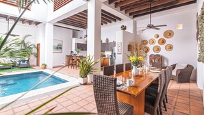 A spacious indoor area with a pool, dining table, wicker chairs, and a ceiling fan. - Casa del Agua Pool House by Xarm Apartments (Santa Marta)