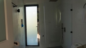 A bathroom with a toilet, shower, and a door leading to an outdoor area.