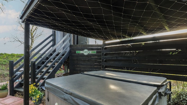 A hot tub under a covered area with a staircase leading up to a gated entrance. - The Carriage Ely Penzance (Ely)