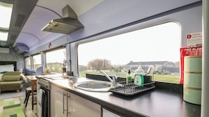 A train's interior kitchen with a sink, countertop, and window view. - The Carriage Ely Penzance (Ely)
