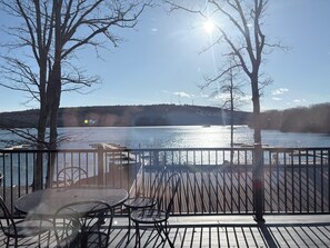 Une terrasse dotée de chaises et de tables en métal, offrant une vue sur une étendue d’eau, avec des arbres et une rive éloignée.