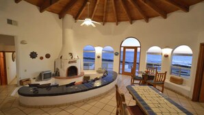 A spacious room with a curved seating area, a fireplace, and large windows offering ocean views. - Charming and Rustic Beachfront Home Sun House (Puerto Peñasco)