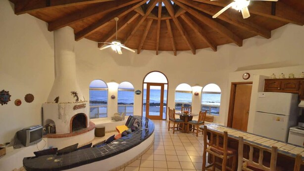 A spacious kitchen with a view of the sea, a fireplace, and a dining area with wooden chairs. - Charming and Rustic Beachfront Home Sun House (Puerto Peñasco)