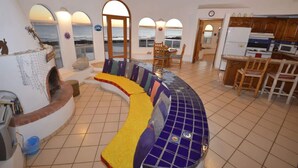 A room with a curved seating area, a kitchen, and a view of the sea through arched windows. - Charming and Rustic Beachfront Home Sun House (Puerto Peñasco)