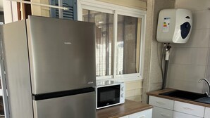 Een kleine keuken met een roestvrijstalen koelkast, een magnetron, witte kasten, een houten aanrecht en een boiler.