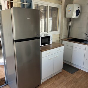 A compact kitchen with a stainless steel refrigerator, a microwave, white cabinets, a wooden countertop, and a water heater. - Mobile home with overhang (Sérignan)