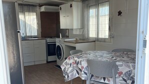 Een kleine keuken met een wasmachine, een eettafel met stoelen en een raam met gordijnen.