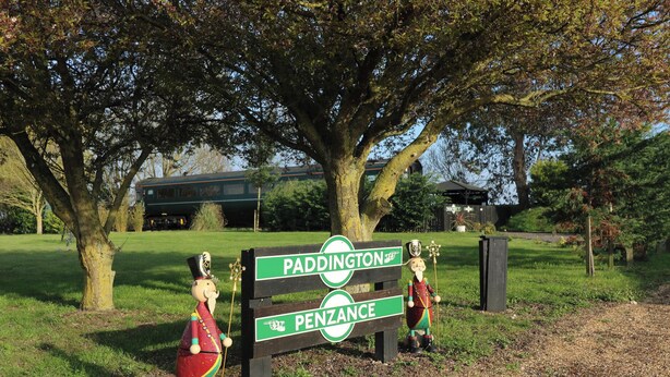 Ein hölzernes Schild mit der Aufschrift 'Paddington' und 'Penzance', verziert mit zwei dekorativen Figuren.