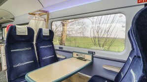 Ein Zugwaggon mit Ersten Klasse Sitzplätzen, einem Tisch und Blick auf die Landschaft.