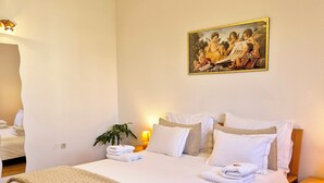 Una cama bien hecha con ropa blanca, un cuadro encima y una lámpara de noche.