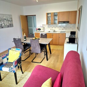 Una cocina compacta con armarios de madera, una mesa de comedor con sillas, un sofá y un cuadro en la pared.