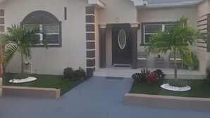 A modern two-story building with a symmetrical facade, a central entrance with a black door, and a well-maintained lawn with palm trees. - Cozy 2-bedroom house where you can "Relax, Recharge, Repeat" (Bodden Town)